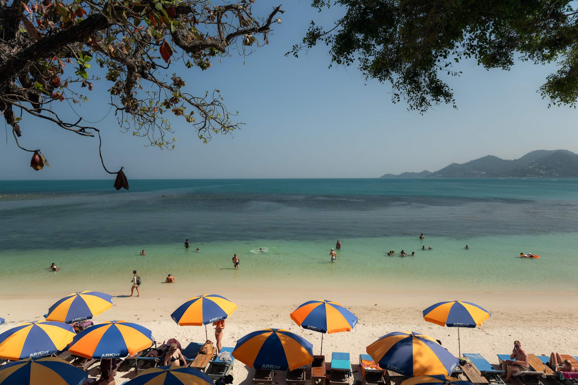 Chaweng Beach Koh Samui clear water swimmers and ARKbar beach club umbrellas with mountain backdrop